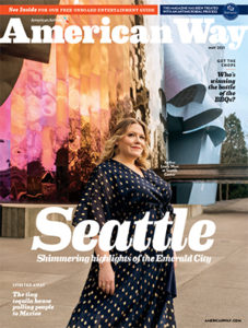 Cover of the penultimate "American Way" magazine for American Airlines. It features writer Liny West in front of the curvy, mirrored plains of Seattle's Museum of Pop Culture. Her blonde hair is down and lightly curled, and she's wearing a navy dress with a white print. The main headline says "Seattle."