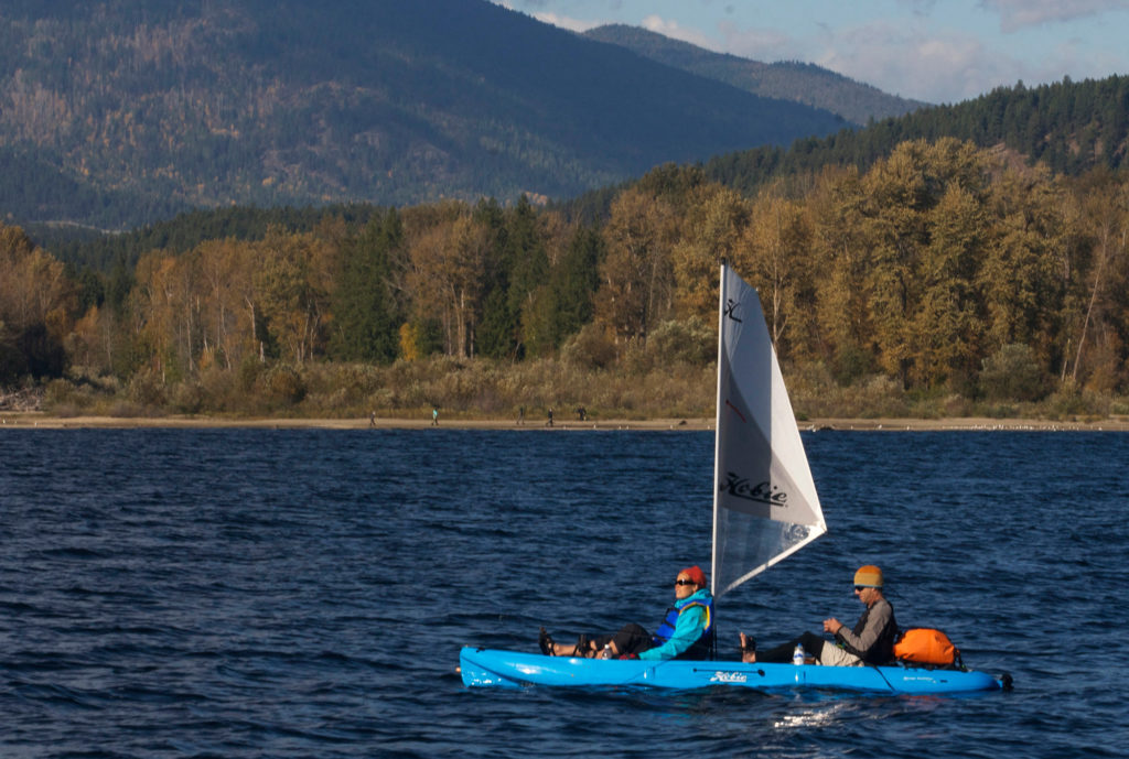 A Hobie fishing kayak sails on a bright blue lake with autumnal mountains in the background