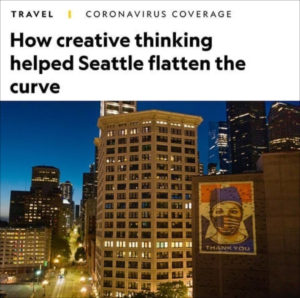 An Instagram capture with "travel" and "coronoavirus coverage" at the top, followed by the National Geographic headline "How creative thinking helped Seattle flatten the curve." The image below shows the city's downtown core at blue hour with Amplifier wheatpaste art of a masked healthcare worker on a skyscraper. Image by Aaron Huey.